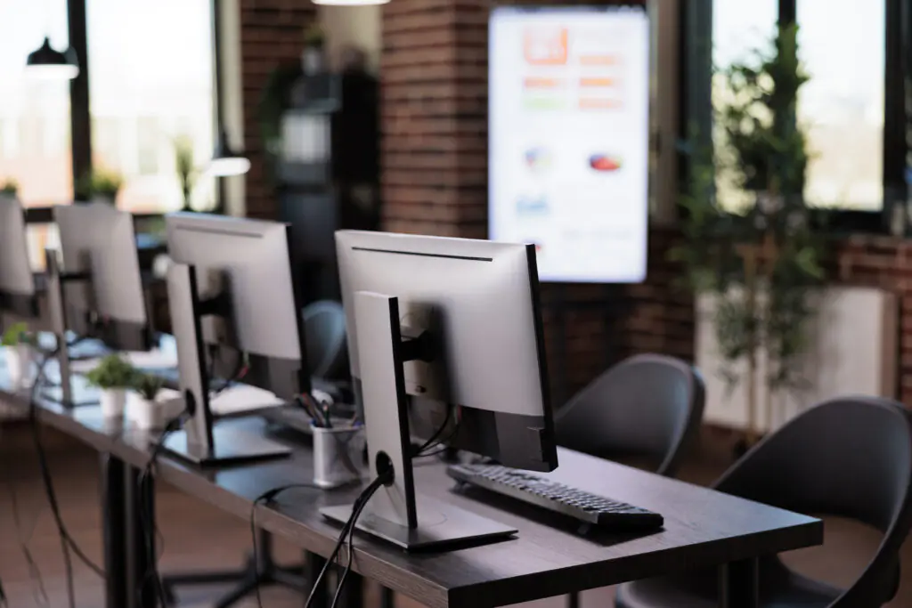 Modern office workspace with rows of computer monitors, keyboards, and plants.