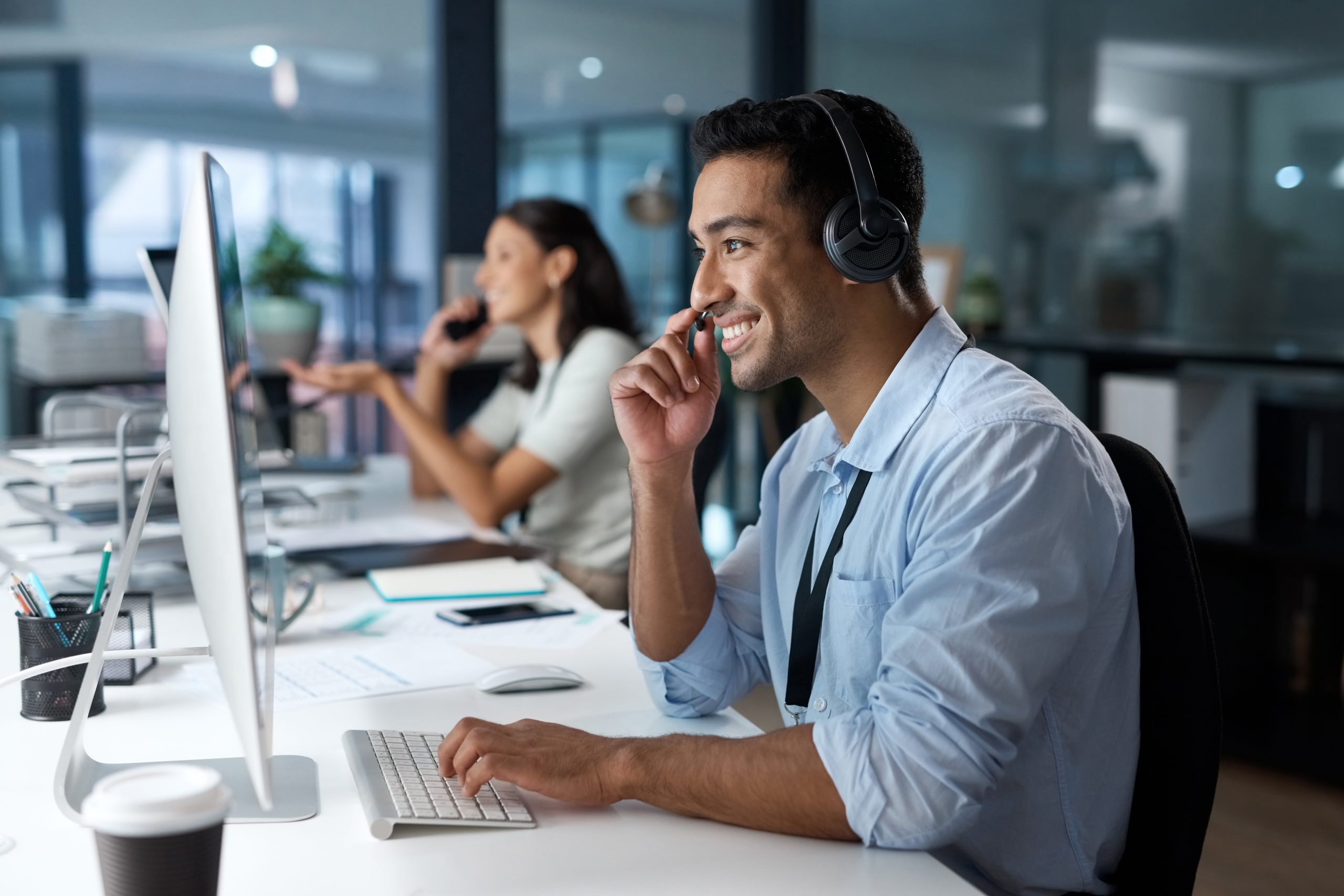 Shot of a young man using a headset and computer in a modern office.